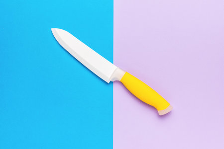 Ceramic white knife with a yellow handle on a violet-blue background. Accessory for cooking. Flat lay.の写真素材