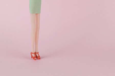Doll women's feet in bright red shoes on a pink background. The concept of female beauty.
