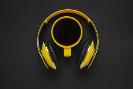 Top view of yellow headphones with a yellow cup of coffee on a black background. The concept of a...
