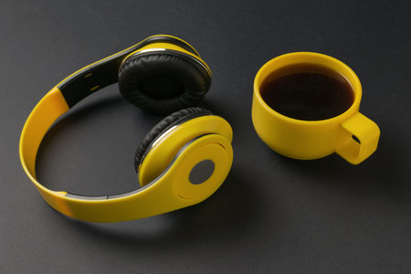 Yellow coffee cup and yellow headphones on a black background. The concept of a stylish workplace.の写真素材
