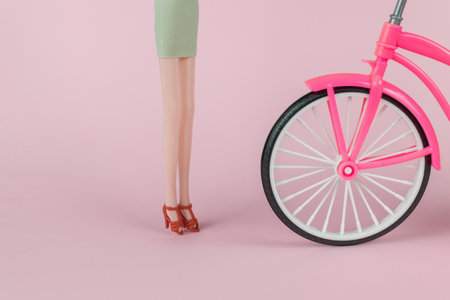 Female doll legs in red shoes next to a bicycle on a pink background. The concept of female beauty.の写真素材