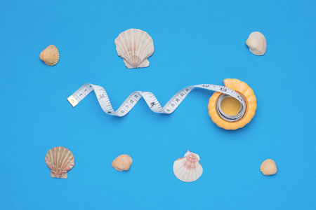 Measuring tape in a shell case and seashells on a blue background. A measurement tool.の写真素材