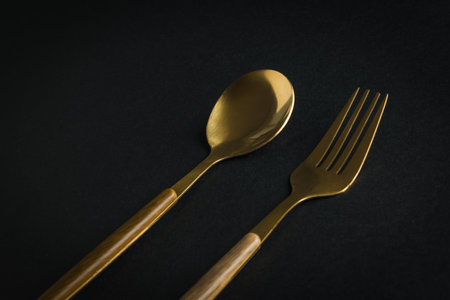 Gold-plated spoon and fork on a black background. Tableware.の写真素材