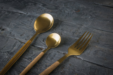 Two gold-plated spoons and a fork on a wooden table. Tableware.
