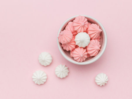 Top view of a white and pink meringue in a white bowl on a pink background. A sweet dish.の写真素材