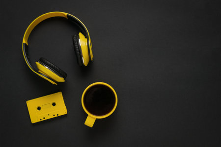 A black background with yellow headphones, a cassette tape and a cup of coffee. The concept of a stylish workplace.の写真素材