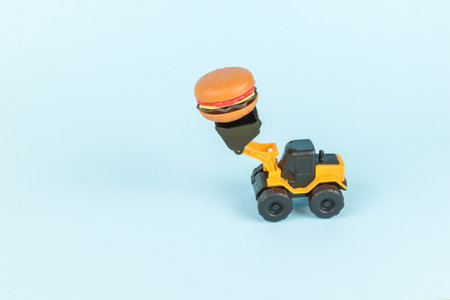 A bulldozer carrying a hamburger on a blue background. Food delivery and disposal.