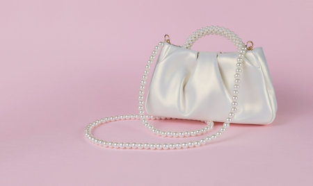 Stylish white women's bag trimmed with pearls on a pink background. A fashionable women's accessory.の写真素材