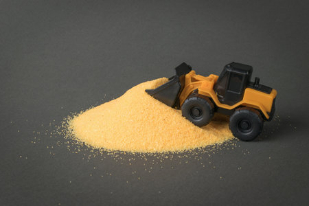A yellow bulldozer is shoveling a large pile of sand. A car for a construction company.
