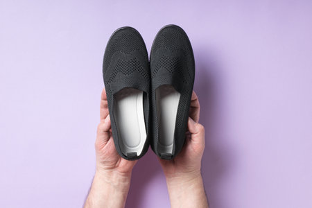A man holds casual women's rag shoes on a purple background. Casual shoes.の写真素材