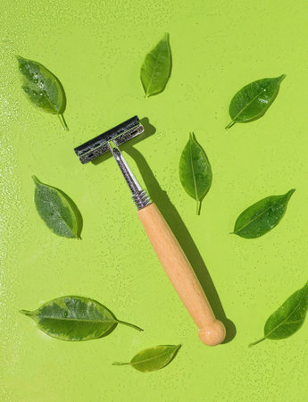 A razor with a wooden handle with green leaves on a green background covered with water. Natural...