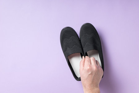 The man's right hand holds cloth women's shoes on a purple background. Casual shoes.の写真素材