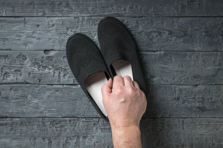 A man's hand with a pair of women's shoes on a wooden background. Casual shoes.の写真素材
