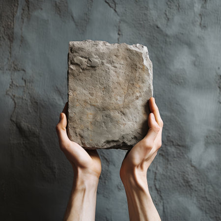 Hands holding a large gray stone on a gray background. The concept of modern art.の素材