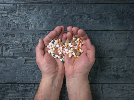 Men's hands with a lot of pills on a wooden background. The need to take medications.の写真素材