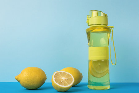 A sports bottle with water and lemon and fresh lemons on a blue background. A refreshing drink for training.の写真素材