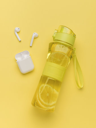 Wireless headphones and a transparent yellow bottle with lemon and ice. Sport concept.の写真素材