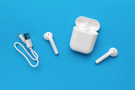 Wireless headphones with charging cable on a blue background. A stylish accessory for listening to audio recordings.の写真素材