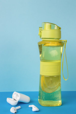 A case with wireless headphones and a sporty yellow water bottle on a blue background. Sport concept.の写真素材