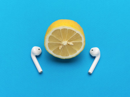 Half a lemon with wireless headphones on a blue background. The concept of listening to music tracks.の写真素材
