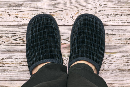 Top view of men's feet in slippers on a light wooden floor. Comfortable home shoes.