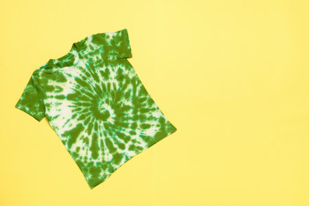 A bright white and green tie dye T-shirt on a yellow background. The concept of making clothes with your own hands.の写真素材