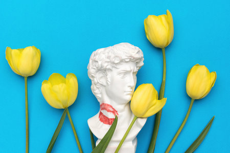 A statue of Apollo with traces of a kiss and yellow tulips on a blue background. The concept of love and romance.の写真素材