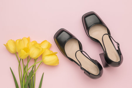 Top view of black women's shoes and a bouquet of yellow tulips on a pink background. The concept of summer and love.の写真素材