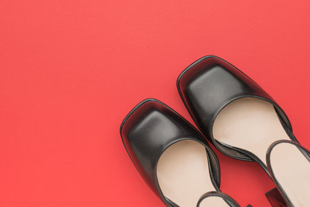 Elegant black formal shoes placed on a vivid red background create a striking contrast, perfect for fashion presentations, advertising materials, or design projects requiring a chic and sophisticated aesthetic.の写真素材