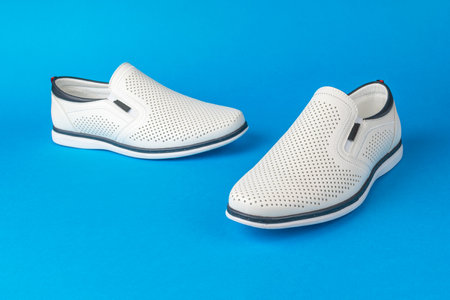 White Slip-On Loafers on Blue Background - Stylish Footwear for Men, Perforated Leather Shoesの写真素材