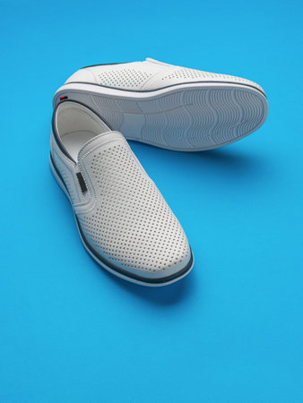 Stylish White Slip-On Sneakers on Vibrant Blue Background - Modern Casual Footwearの写真素材