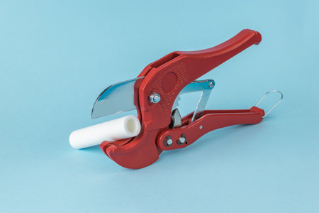 Red Pipe Cutter with White PVC Pipe on Blue Background - Plumbing Toolの写真素材