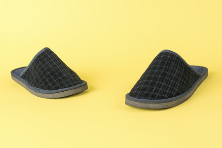 Comfortable Black Slippers on Yellow Background - Cozy Home Footwear for Relaxed Indoor Wearの写真素材