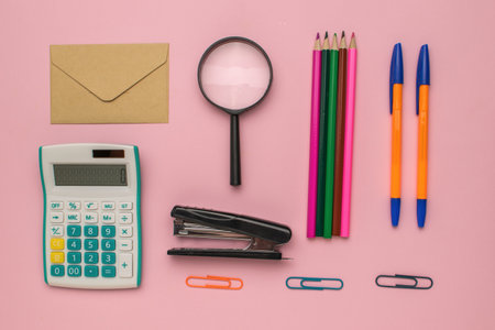 Office Supplies on Pink Background: Calculator, Magnifier, Stapler, Pens, Pencils, Envelope, and Paper Clipsの写真素材