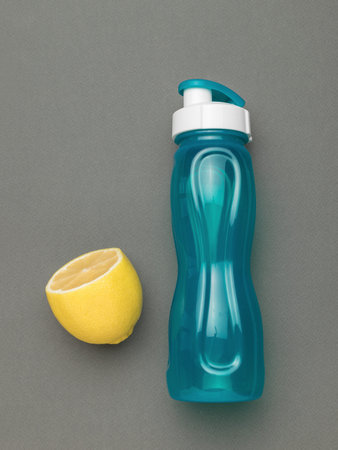Hydration and Freshness: Blue Water Bottle with Lemon Half on Gray Backgroundの写真素材