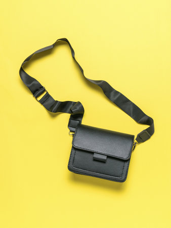 Black Leather Crossbody Bag on Yellow Background - Modern Fashion Accessory for Everyday Useの写真素材