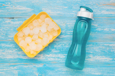 Reusable Water Bottle and Ice Cube Tray on Weathered Blue Wooden Surfaceの写真素材