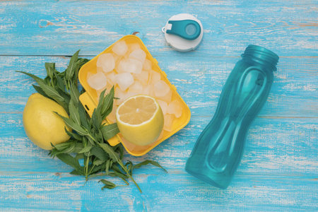 Refreshing Summer Lemonade Preparation with Fresh Lemons, Ice, and Water Bottle on Blue Wooden Backgroundの写真素材