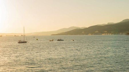 Tranquil Coastal Scene with Boats and Mountains at Sunsetの写真素材