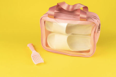 Pink Travel Toiletry Bag with Brush on Yellow Background - Clear Plastic Cosmetic Organizer for Travel Essentialsの写真素材