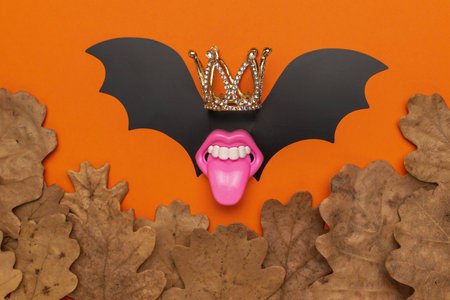 Creative Halloween Concept with Crowned Bat Wings, Pink Lips and Autumn Leaves on Orange Backgroundの写真素材