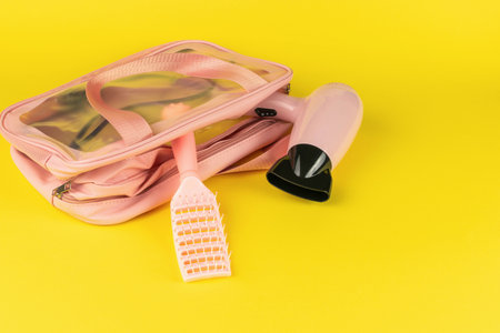 Pink Hair Dryer and Comb in Transparent Travel Bag on Yellow Backgroundの写真素材