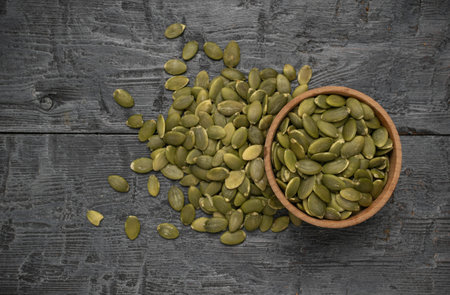 Bowl and Scattered Pumpkin Seeds on Rustic Wooden Surfaceの写真素材