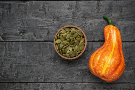 Rustic Display of Pumpkin Seeds in Wooden Bowl and Colorful Pumpkin on Dark Wooden Backgroundの写真素材