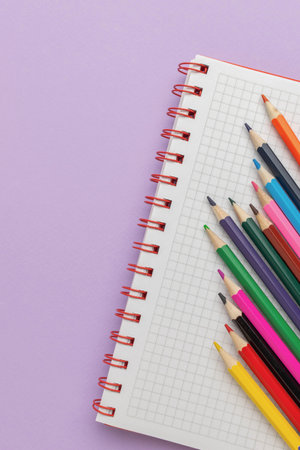 Colorful Pencils Arranged on Graph Notebook with Purple Background for Artistic and Educational Conceptの写真素材
