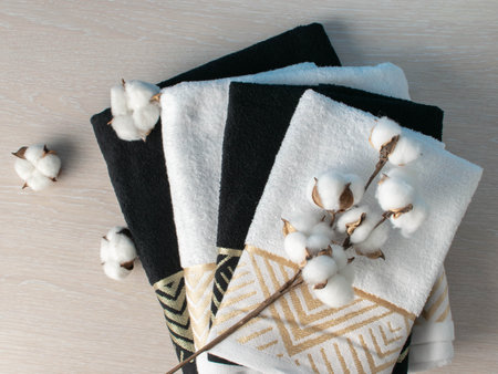 ** Elegant Black and White Towels with Decorative Gold Accents and Cotton Branch on Wooden Surfaceの写真素材