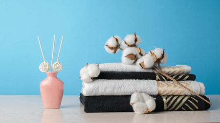 Spa Towels and Cotton Branch with Aromatic Diffuser on Light Wooden Table against Blue Backgroundの写真素材