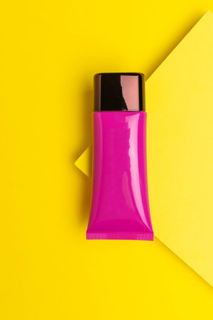 Bright Pink Cosmetic Tube on Vibrant Yellow Background - Minimalist Skincare Packagingの写真素材