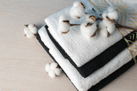 Stacked Black and White Towels with Cotton Flowers on Light Wood Backgroundの写真素材