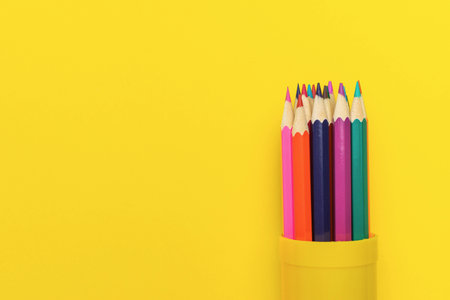 Colorful Pencils in Yellow Container on Bright Yellow Background - Vibrant Stationeryの写真素材
